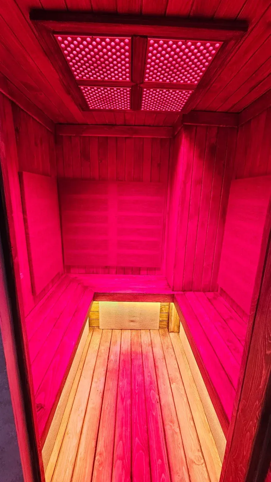Bên trong phòng xông hồng ngoại với băng ghế gỗ và tấm đèn đỏ tại Ōmni Space – inside the infrared sauna with wooden benches and red-light panels at Ōmni Space