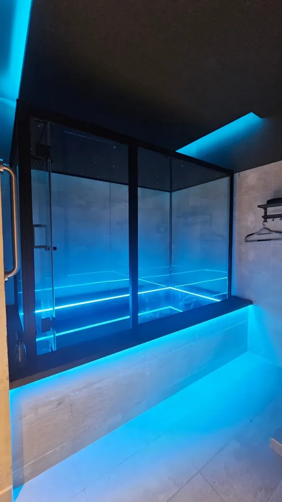 Phòng float kính với đèn xanh dịu tại Ōmni Space – The glass float room in soft blue light at Ōmni Space