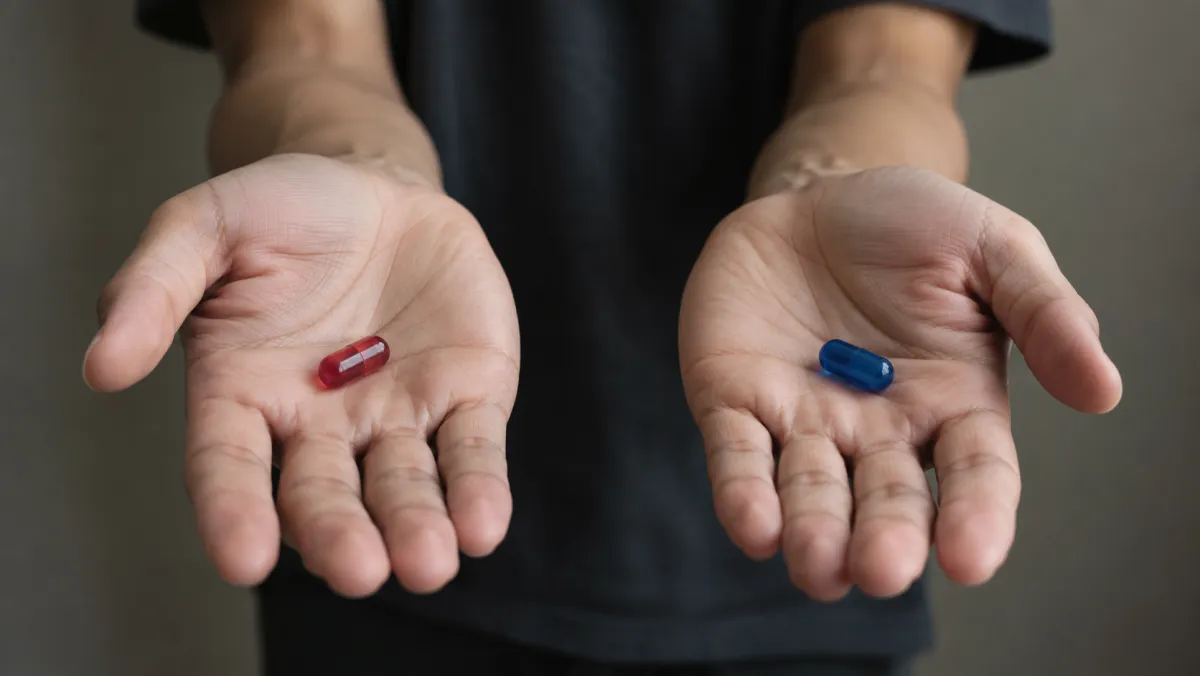 Hai bàn tay cầm một viên thuốc đỏ và một viên thuốc xanh – two hands holding a red pill and a blue pill